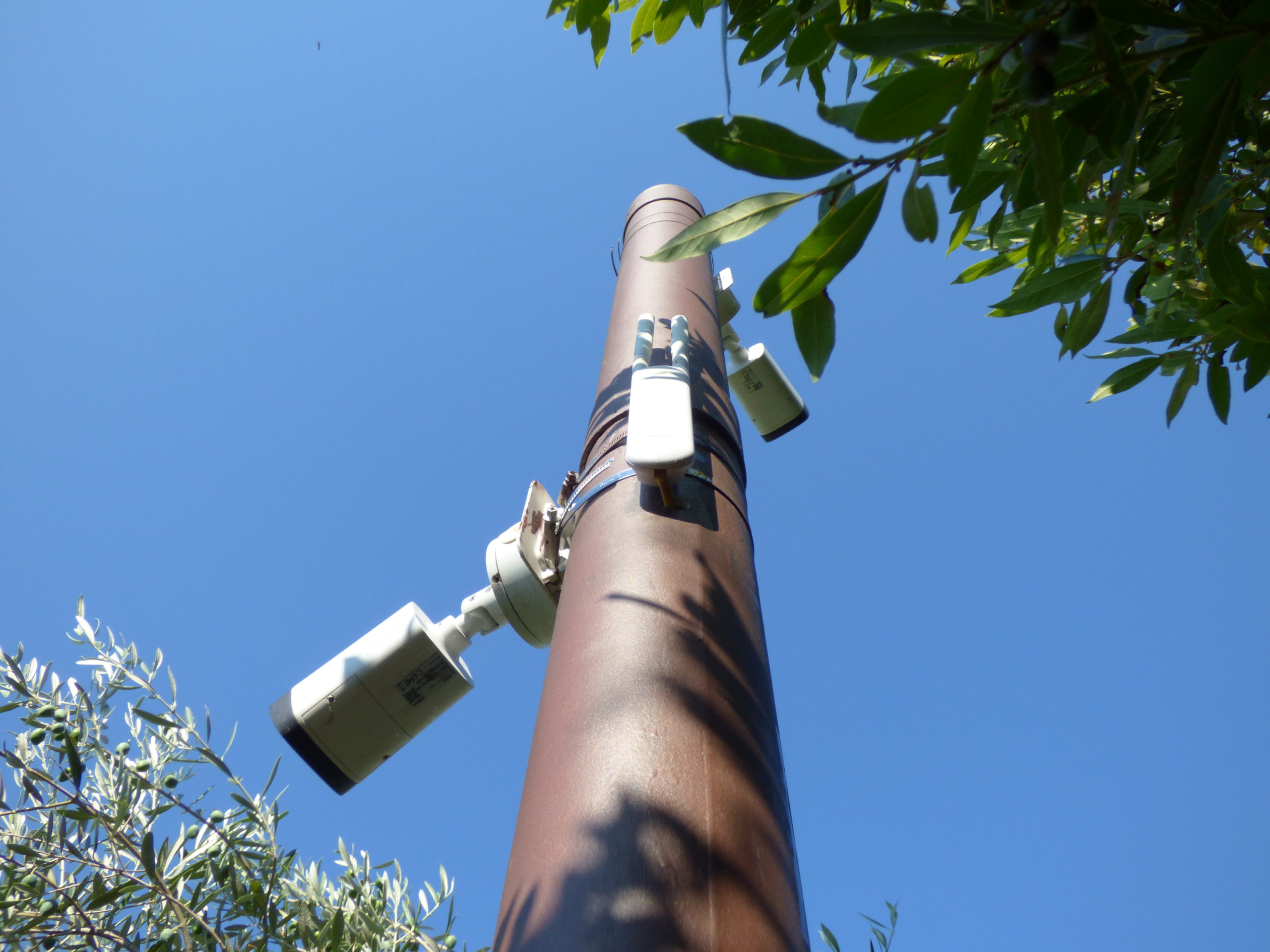 Caméra de vidéosurveillance tube sur un poteau surveillant les extérieurs d'une villa. Il y a aussi une borne wifi pour capter internet dans le jardin.